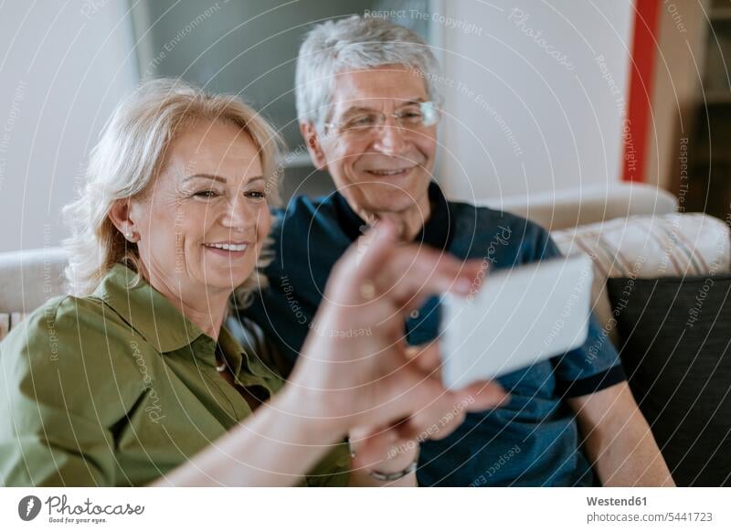 Älteres Paar zu Hause auf der Couch sitzend und ein Selfie machend Selfies Handy Mobiltelefon Handies Handys Mobiltelefone Pärchen Paare Partnerschaft Sofa