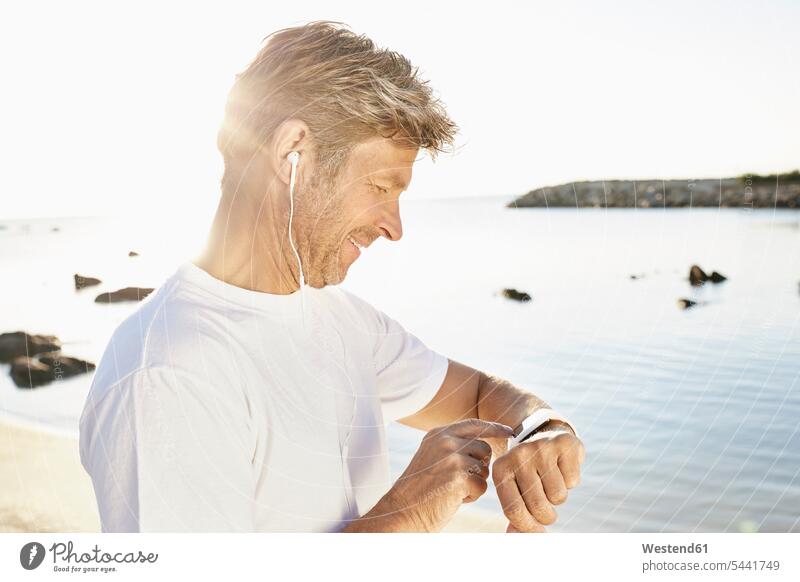 Reifer Mann mit Kopfhörer, der nach dem Joggen am Strand seine Smartwatch überprüft Männer männlich Erwachsener erwachsen Mensch Menschen Leute People Personen