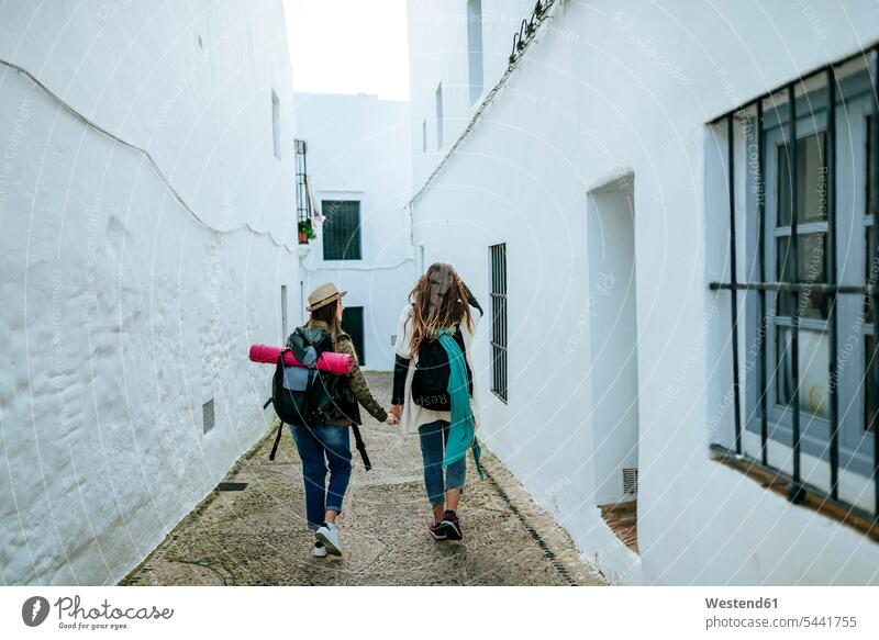 Zwei junge Frauen auf einem Spaziergang in einer Stadt, die Händchen halten Freundinnen gehen gehend geht Freunde Freundschaft Kameradschaft Touristin