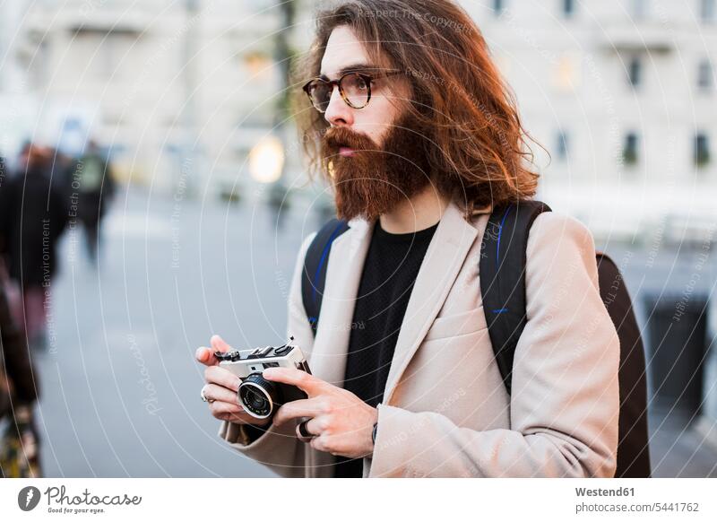 Stylischer junger Mann im Freien, der eine Kamera hält und sich umsieht halten Fotograf Fotografen Photographen Männer männlich Fotoapparat Fotokamera