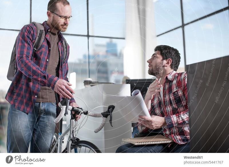 Lässiger Mann mit Fahrrad im modernen Büro im Gespräch mit Kollege Männer männlich Bikes Fahrräder Räder Rad Kollegen Arbeitskollegen Office Büros Erwachsener