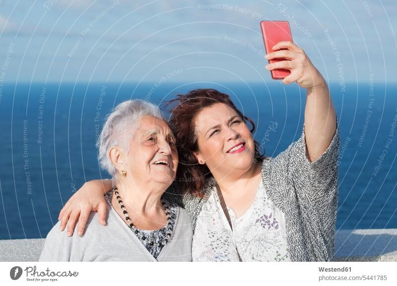Großmutter und Enkelin machen ein Selfie vor dem Meer Enkeltochter Enkelinnen Enkeltöchter Grossmutter Oma Grossmama Großmütter Omi Portrait Porträts Portraits
