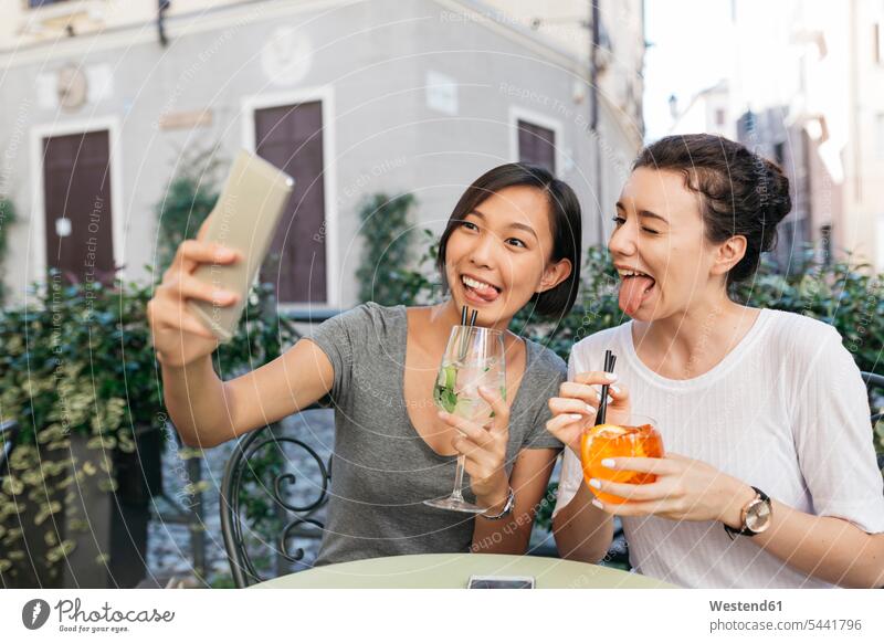 Italien, Padua, zwei junge Frauen, die bei einem Selfie in einem Straßencafé lustige Gesichter machen Freundinnen Selfies Freunde Freundschaft Kameradschaft