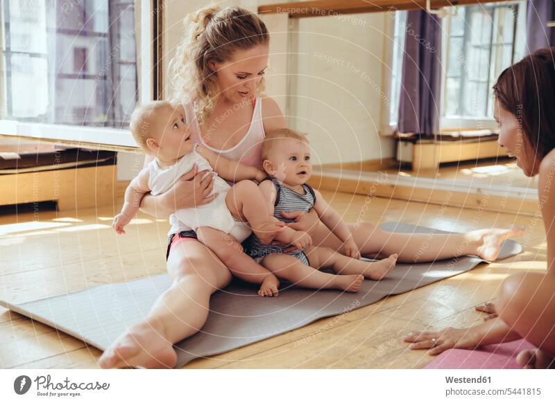 Mutter mit Zwillingsbabys auf Yogamatte sitzend Mami Mutti Mütter Mama lächeln Baby Babies Babys Säuglinge Kind Kinder trainieren Spaß Spass Späße spassig