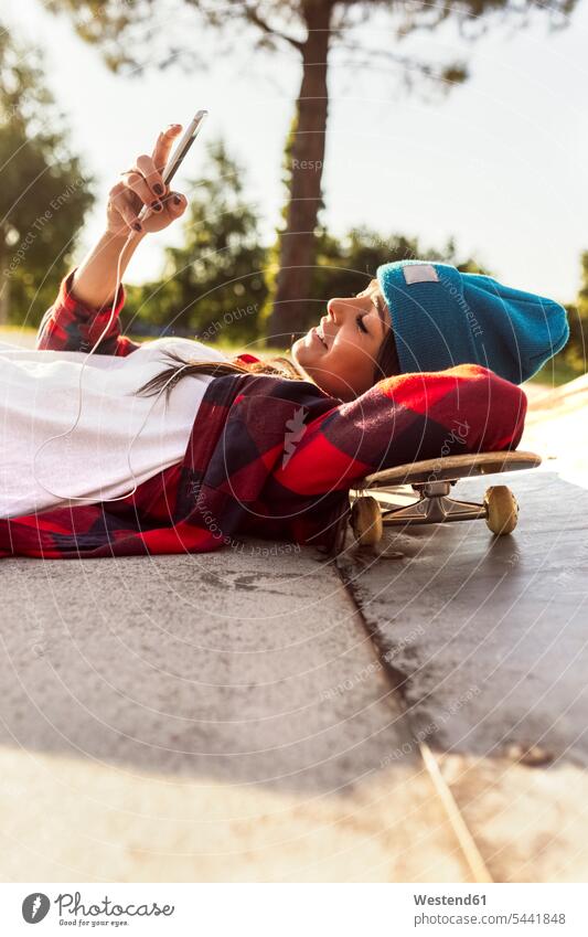Junge Frau liegt auf Skateboard und schaut auf Handy liegen liegend lächeln Rollbretter Skateboards Mobiltelefon Handies Handys Mobiltelefone weiblich Frauen