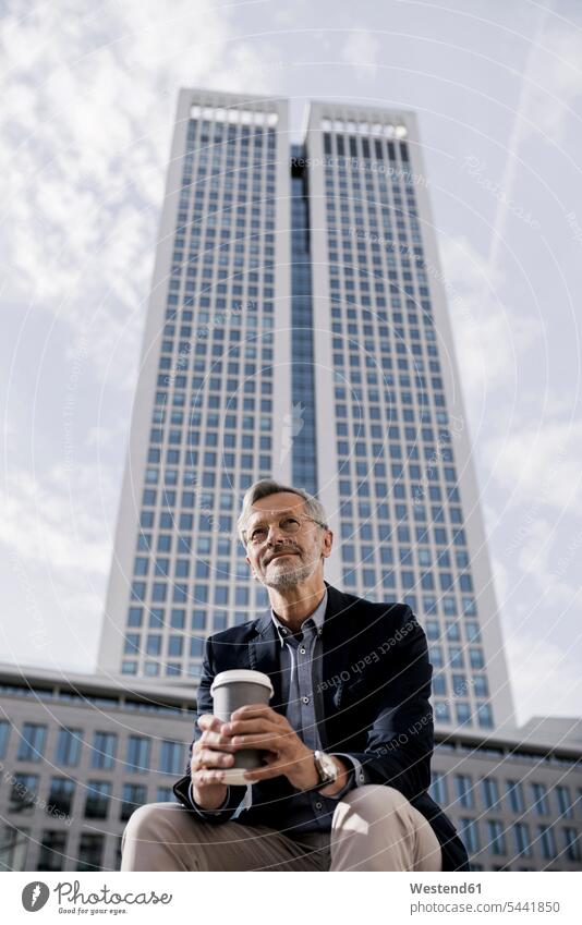 Grauhaariger Geschäftsmann vor einem Wolkenkratzer mit Kaffee zum Mitnehmen sitzen sitzend sitzt Businessmann Businessmänner Geschäftsmänner Hochhaus Skycrapers