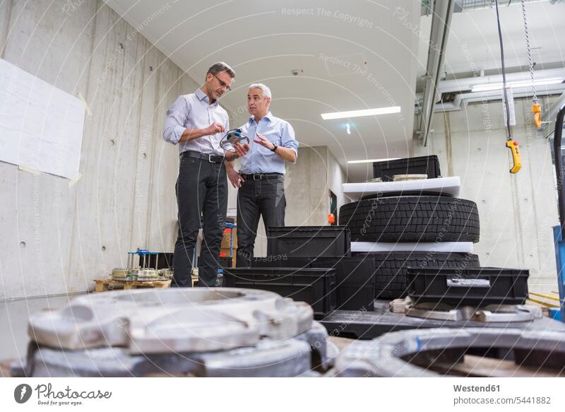 Zwei Geschäftsleute in Fabrikhalle mit Reifen untersuchen Produkt sprechen reden Fabriken arbeiten Arbeit Kollegen Arbeitskollegen Mann Männer männlich