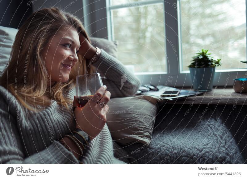 Lächelnde blonde Frau mit einem Glas Kaffee, die sich zu Hause auf der Couch entspannt weiblich Frauen Sofa Couches Liege Sofas Erwachsener erwachsen Mensch