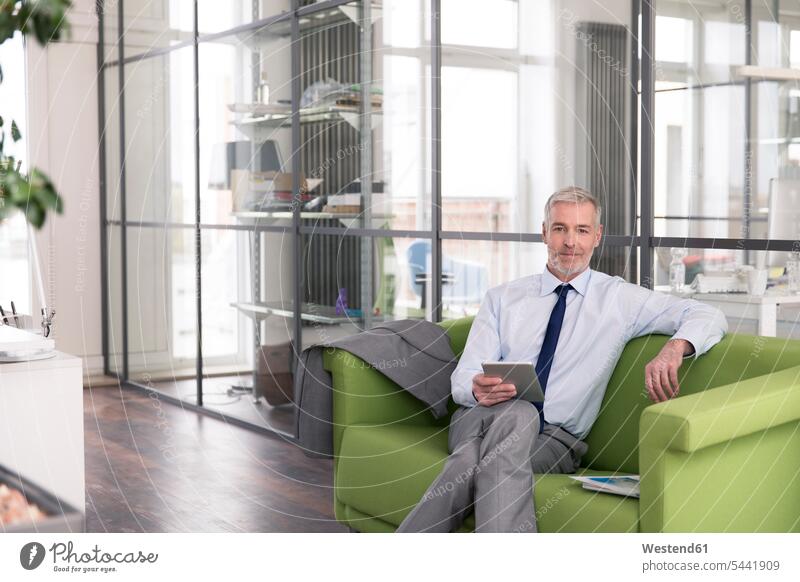 Ein reifer Geschäftsmann sitzt im Büro auf einer Couch und hält ein digitales Tablet Europäer Kaukasier Europäisch kaukasisch Zuversicht Zuversichtlich
