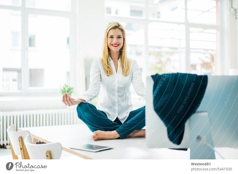 Lächelnde Geschäftsfrau sitzt im Büro auf dem Schreibtisch und praktiziert Yoga Geschäftsfrauen Businesswomen Businessfrauen Businesswoman Office Büros