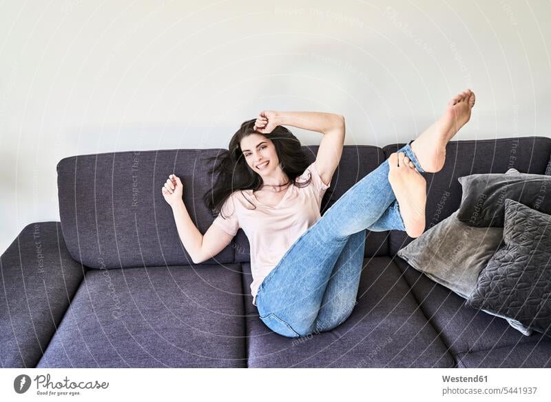 Verspielte junge Frau amüsiert sich auf der Couch Spaß Spass Späße spassig Spässe spaßig entspannt entspanntheit relaxt weiblich Frauen lachen Entspannung