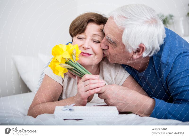 Älteres Ehepaar liegt im Bett, Mann schenkt der Frau einen Blumenstrauß Europäer Kaukasier Europäisch kaukasisch Unbeschwert Sorglos Betten Beziehung lächeln