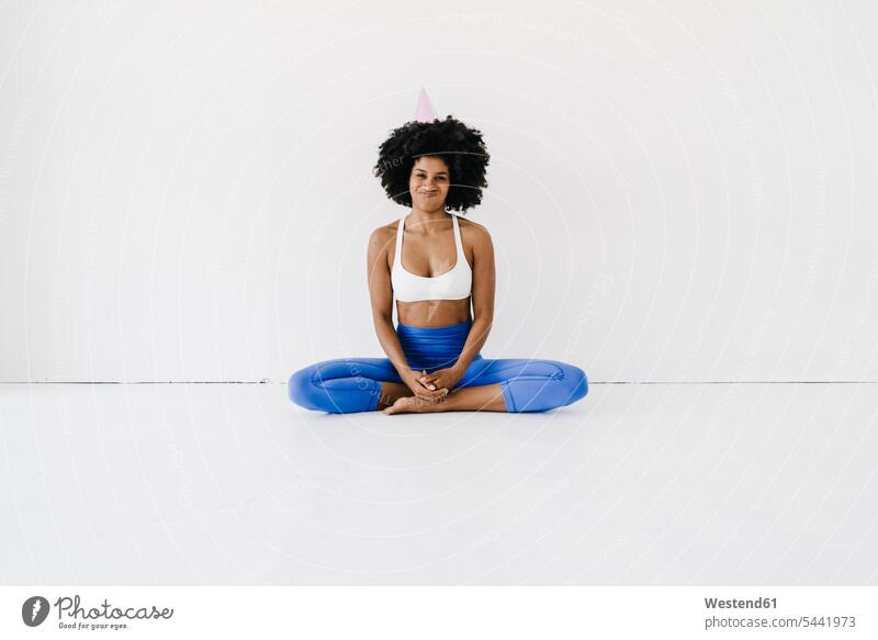 Junge Frau sitzt im Lotussitz und trägt einen Parteihut Yoga Training trainieren weiblich Frauen Schneidersitz fit sitzen sitzend Erwachsener erwachsen Mensch