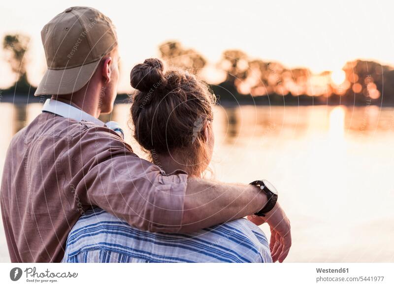 Junges Paar beobachtet den Sonnenuntergang über einem Fluss Pärchen Paare Partnerschaft Aussicht Ausblick Ansicht Überblick Sonnenuntergänge Mensch Menschen