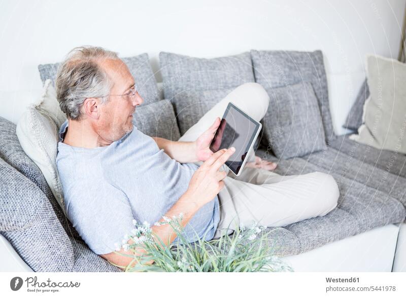 Reifer Mann zu Hause auf dem Sofa liegend mit digitalem Tablett Männer männlich Couches Liege Sofas entspannt entspanntheit relaxt Tablet Computer Tablet-PC