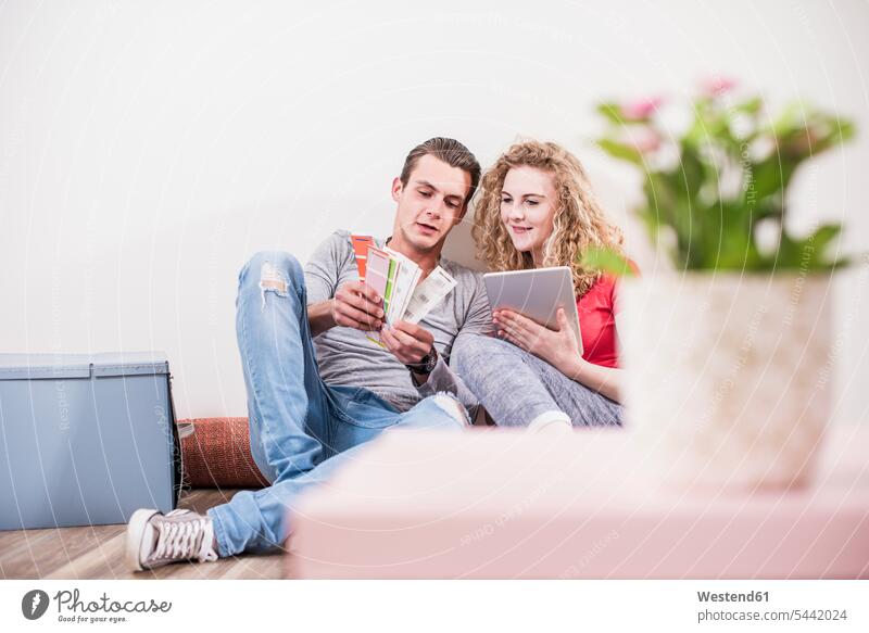 Junges Paar in neuer Wohnung sitzt auf dem Boden sitzend mit Tablette, die aus einem Farbmuster ausgewählt wird wohnen Wohnungen Pärchen Paare Partnerschaft
