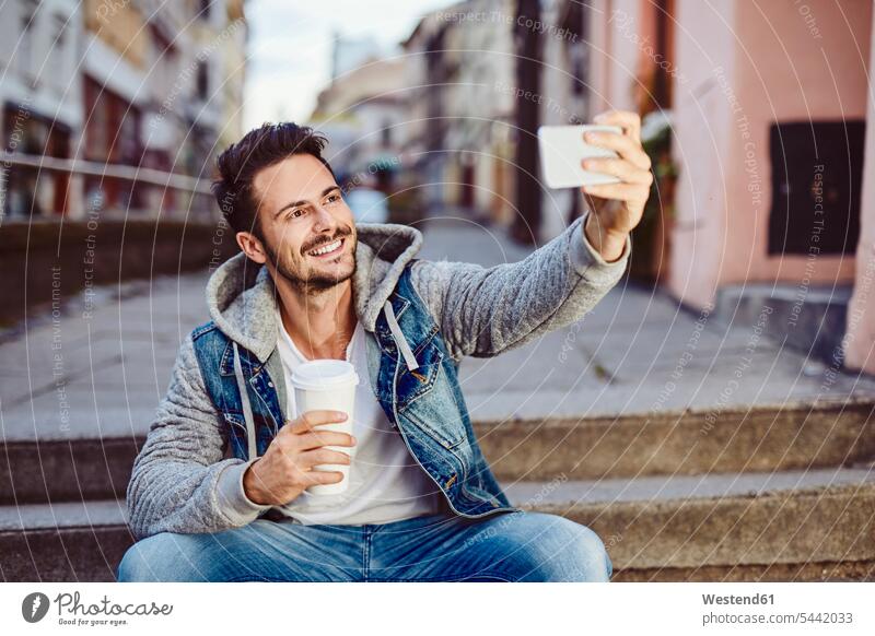 Mann macht Selfie mit Kaffee und sitzt auf einer Treppe Selfies Handy Mobiltelefon Handies Handys Mobiltelefone lächeln Männer männlich sitzen sitzend glücklich