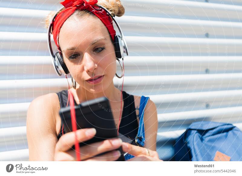 Porträt einer jungen Frau mit Kopfhörern, die auf ein Smartphone schaut weiblich Frauen iPhone Smartphones Kopfhoerer Erwachsener erwachsen Mensch Menschen
