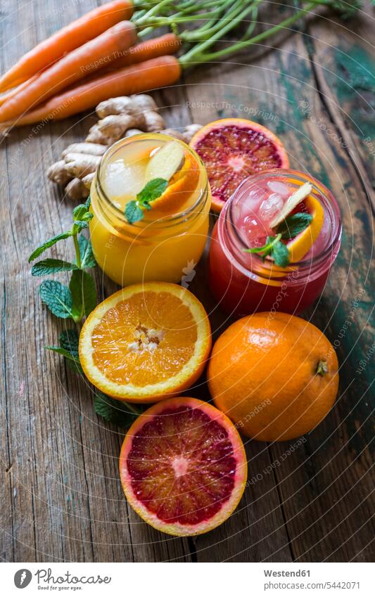 Zwei Gläser mit verschiedenen Orangensäften, Orangen, Karotten, Minzblättern und Ingwer eisgekühlt eisgekuehlt eisgekühlte aufgeschnitten Scheibe angeschnitten