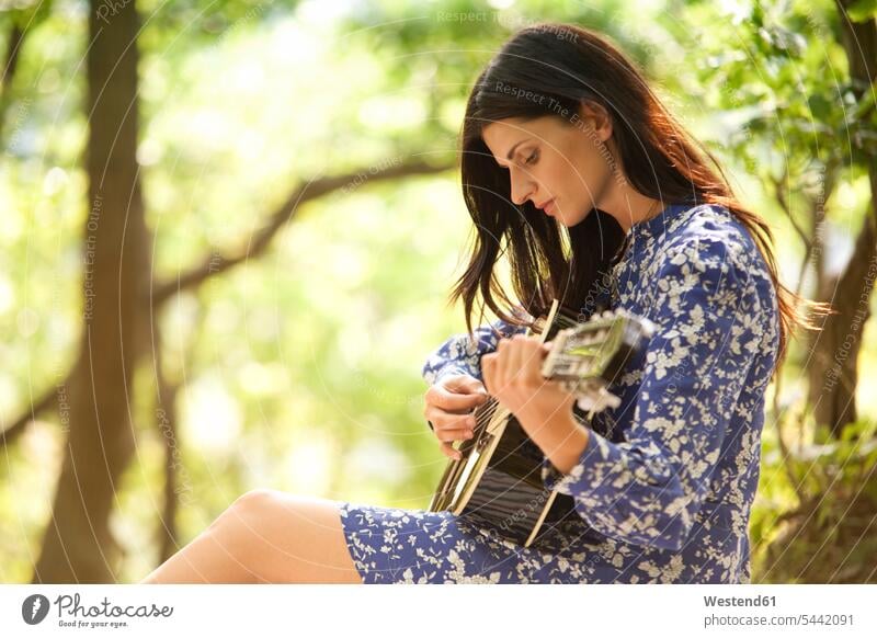 Junge Frau spielt Gitarre im Wald Gitarren Forst Wälder weiblich Frauen Saiteninstrument Saiteninstrumente Musikinstrument Musikinstrumente Instrumente