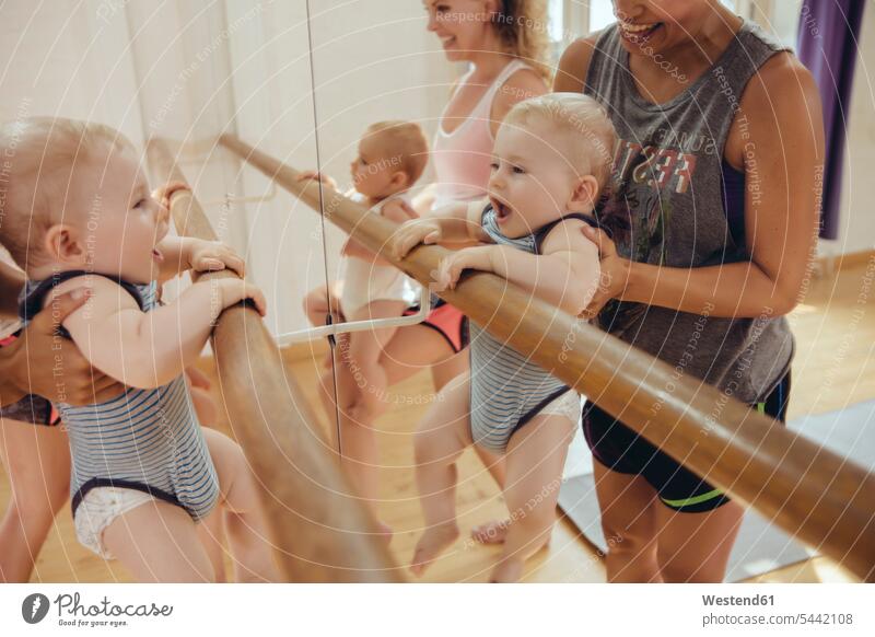 Zwei Mütter, die ihre kleinen Kinder im Tanzstudio zum Barren halten Spiegel Mutter Mami Mutti Mama lächeln Baby Babies Babys Säuglinge Spaß Spass Späße spassig