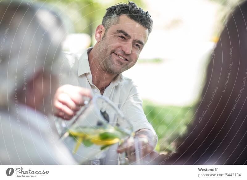 Lächelnder Mann gießt im Garten Limonade ins Glas feiern Freunde eingießen schütten einschenken schuetten lächeln Gruppe Gruppe von Menschen Menschengruppe