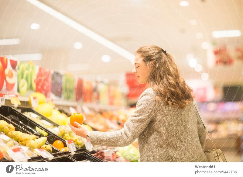 Junge Frau wählt Kaki im Supermarkt Supermaerkte Supermärkte aussuchen auswählen Sharonfrüchte Kakis Sharonfrucht Kakifrucht Sharons Persimon Kakifrüchte