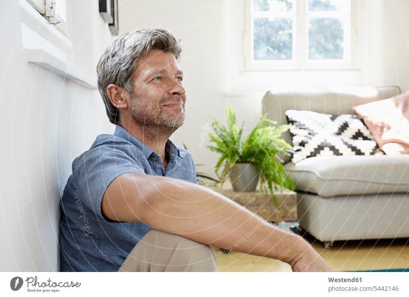 Reifer Mann zu Hause vor der Couch sitzend sitzt auf dem Boden sitzen auf dem Boden sitzend Männer männlich Zuhause daheim Erwachsener erwachsen Mensch Menschen