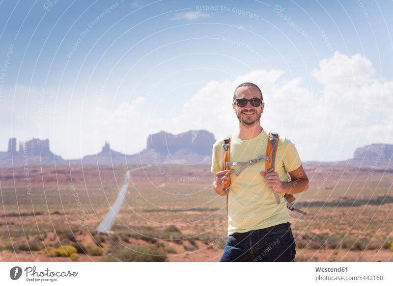 USA, Utah, Porträt eines lächelnden Mannes mit Rucksack und Sonnenbrille auf dem Weg zum Monument Valley Männer männlich Portrait Porträts Portraits Erwachsener