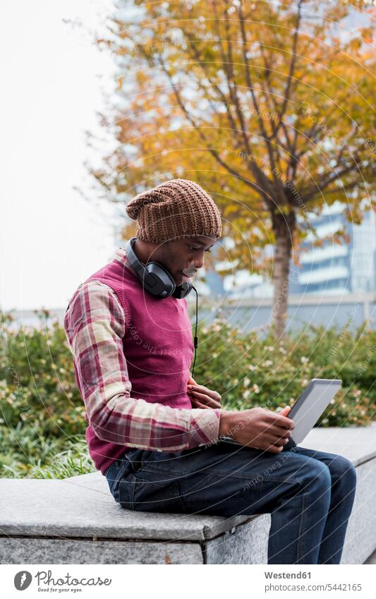 Mann mit Kopfhörern sitzt auf Bank und schaut auf Laptop Notebook Laptops Notebooks Männer männlich Computer Rechner Erwachsener erwachsen Mensch Menschen Leute