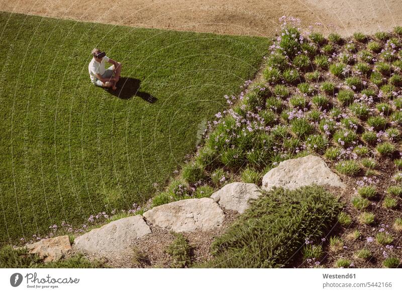 Mann mit VR-Brille sitzt auf Rasen im Garten Brillen Männer männlich Virtuelle Realität Virtuelle Realitaet Gärten Gaerten sitzen sitzend Gras Erwachsener
