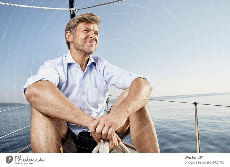 Porträt eines lächelnden reifen Mannes, der auf seinem Segelboot sitzt und in die Ferne schaut Männer männlich Segeln segelnd segelt Erwachsener erwachsen
