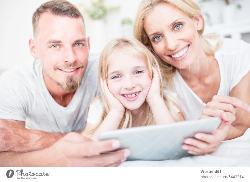 Porträt eines lächelnden Mädchens, dessen Eltern mit einer Tablette im Bett liegen Tochter Töchter Betten Familie Familien Tablet Computer Tablet-PC Tablet PC