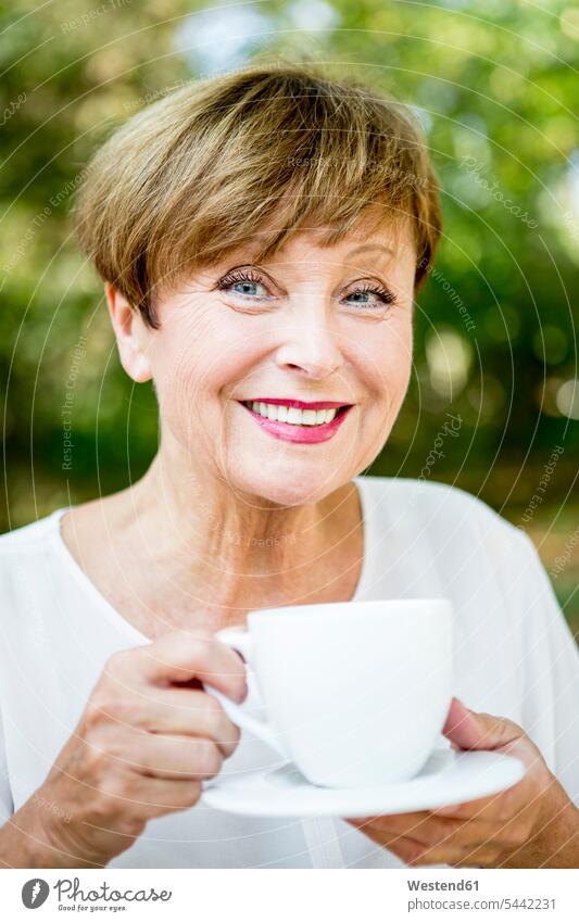 Porträt einer lächelnden älteren Frau, die im Freien eine Tasse Kaffee trinkt weiblich Frauen Getränk Getraenk Getränke Getraenke Food and Drink Lebensmittel