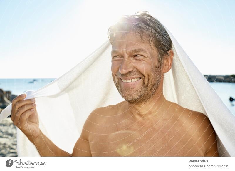 Porträt eines lächelnden Mannes mit Handtuch vor dem Meer Strand Beach Straende Strände Beaches Männer männlich Portrait Porträts Portraits Erwachsener