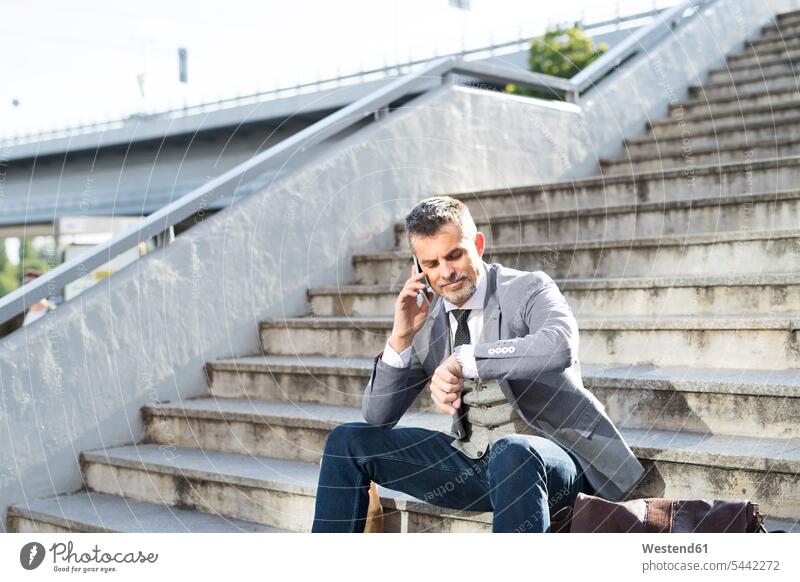 Geschäftsmann in der Stadt sitzt am Handy und überprüft die Uhrzeit Businessmann Businessmänner Geschäftsmänner Pause Treppe Treppenaufgang Geschäftsleute