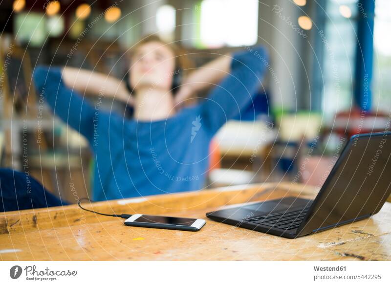 Laptop und Smartphone auf dem Tisch mit entspannendem jungen Mann, der im Hintergrund Musik hört Notebook Laptops Notebooks iPhone Smartphones Student