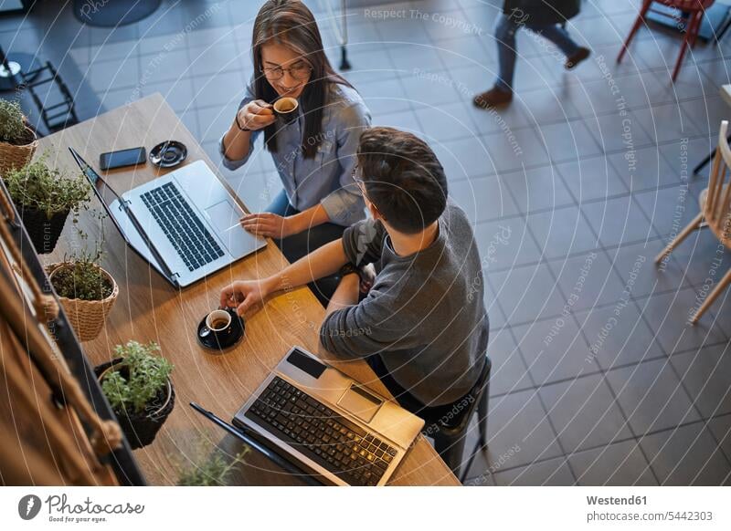Junge Frau und Mann in einem Café mit Laptops unterhalten sich und trinken Espresso Expresso Notebook Notebooks Männer männlich Cafe Kaffeehaus Bistro Cafes