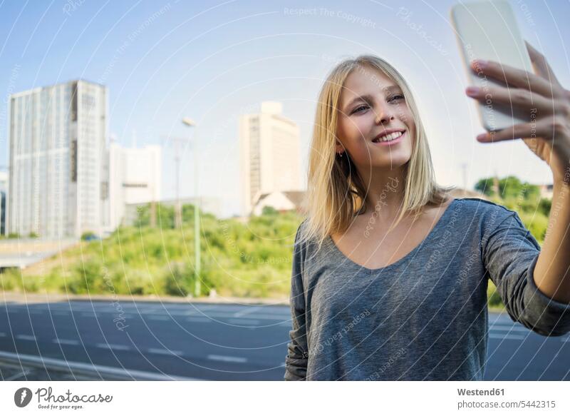 Porträt einer lächelnden jungen Frau, die ein Selfie mit ihrem Smartphone macht weiblich Frauen iPhone Smartphones Selfies Portrait Porträts Portraits