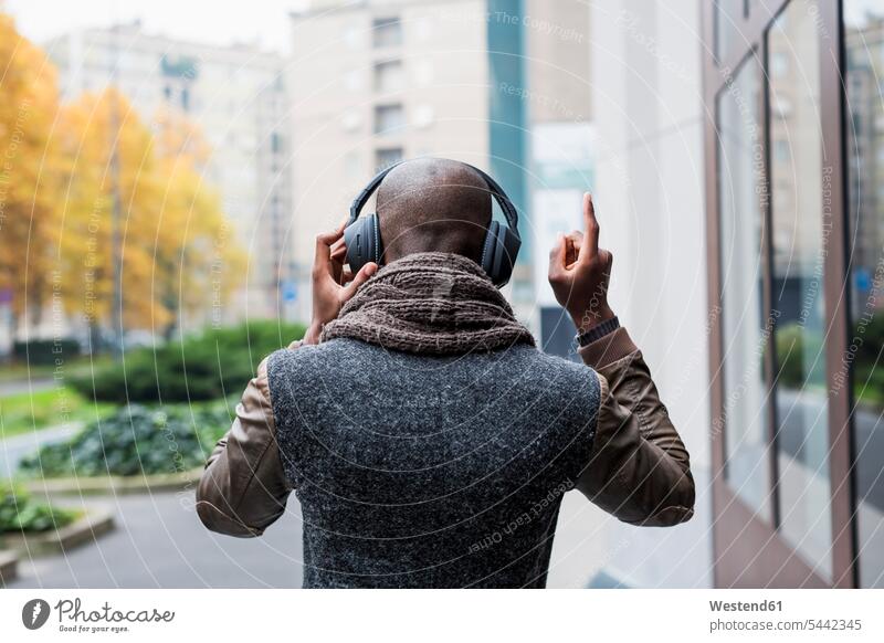 Rückenansicht eines kahlköpfigen Mannes, der mit Kopfhörern Musik hört Kopfhoerer Männer männlich Erwachsener erwachsen Mensch Menschen Leute People Personen