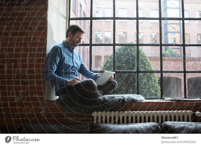 Erwachsener Mann sitzt auf der Fensterbank und benutzt einen Laptop Notebook Laptops Notebooks arbeiten Arbeit sitzen sitzend Zuhause zu Hause daheim