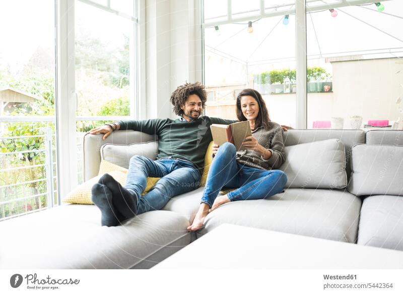 Paar sitzt auf der Couch und liest Buch Sofa sitzen Mensch Hobby glücklich Schwarze Vorstellungskraft Wissen Freizeit offenes Lächeln Zuversicht Textfreiraum