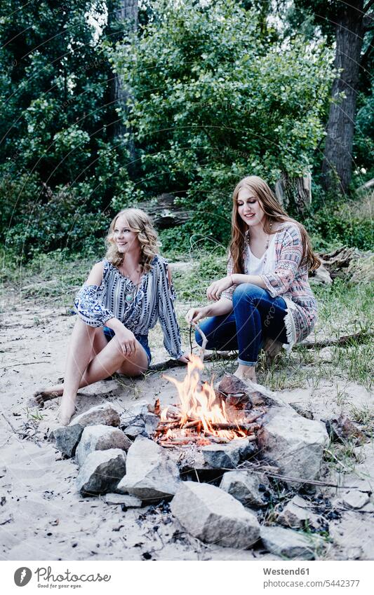 Zwei Teenager-Mädchen sitzen am Lagerfeuer Freundinnen Strand Beach Straende Strände Beaches Feuer Freunde Freundschaft Kameradschaft lächeln Teenagerin
