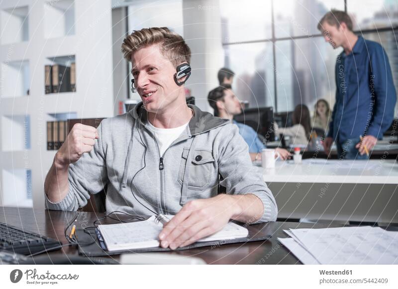 Junger Mann am Schreibtisch im Büro mit einem Headset Headsets Office Büros Männer männlich telefonieren anrufen Anruf telephonieren Call Center Callcenters