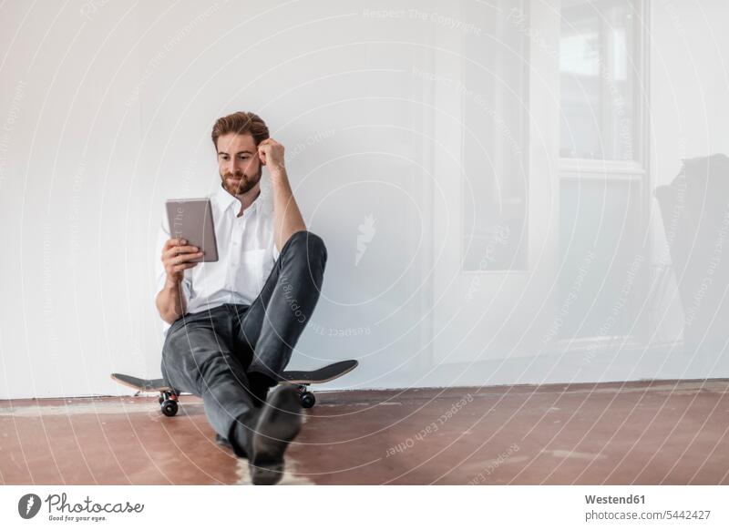 Porträt eines jungen Geschäftsmannes, der auf einem Skateboard auf dem Boden sitzt Businessmann Businessmänner Geschäftsmänner Tablet Tablet Computer Tablet-PC