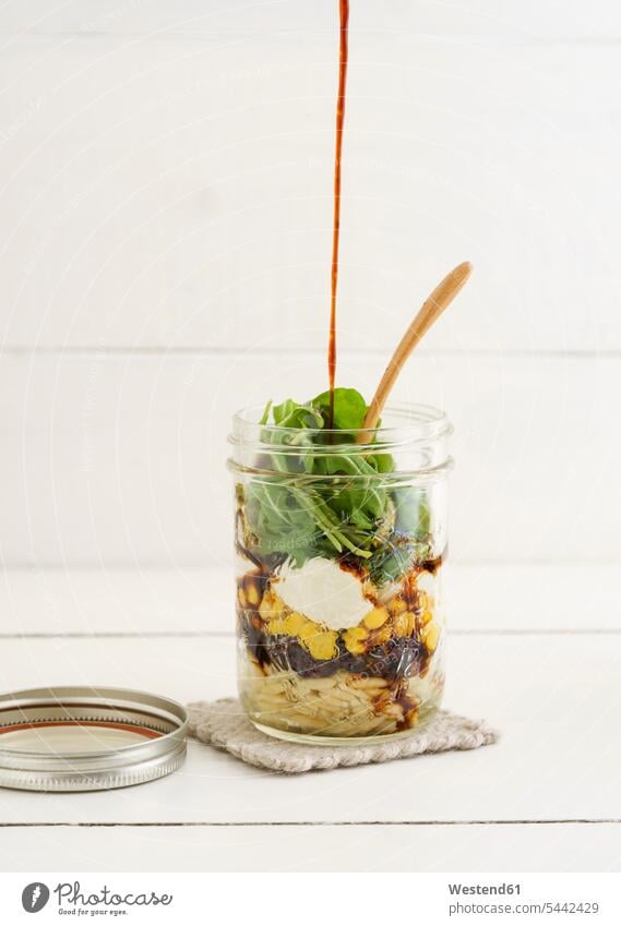 Glas gemischter vegetarischer Salat mit Kritharaki, Mais, Rucola, Preiselbeeren und Balsamico-Essig weißer Hintergrund weisser Hintergrund Salate hölzern
