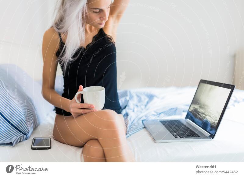 Junge Frau im Bett mit Tasse Kaffee und Laptop Notebook Laptops Notebooks Kaffeetasse Kaffeetassen Betten weiblich Frauen Getränk Getraenk Getränke Getraenke