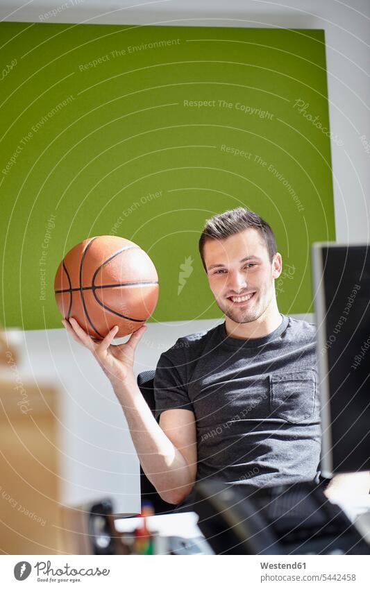 Junger Mann arbeitet im Büro und balanciert einen Basketball arbeiten Arbeit Portrait Porträts Portraits Ball Bälle balancieren Balance Office Büros lächeln