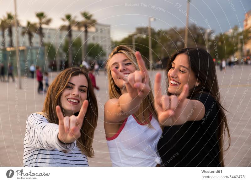 Spanien, Barcelona, drei glückliche junge Frauen zeigen Rock And Roll-Zeichen Freundinnen Freunde Freundschaft Kameradschaft Hörnerzeichen Teufelshörner
