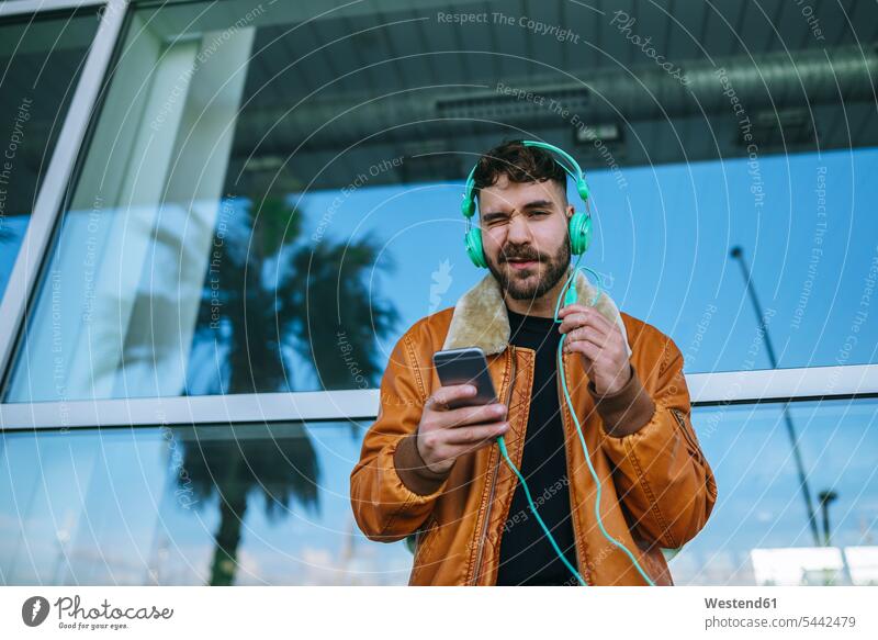 Spanien, Cádiz, Junger Mann am Hafen mit Smartphone, Kopfhörer tragend Lederjacke Lederjacken unterwegs auf Achse in Bewegung Freizeitkleidung casual